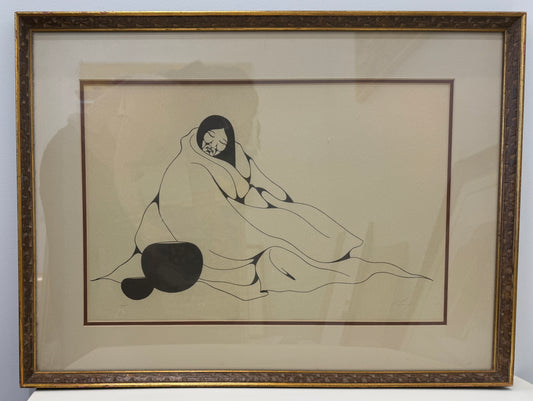 A framed black-and-white drawing titled "Indian Woman 10/25" depicts a person sitting wrapped in a blanket, with two round objects nearby against a plain background. The artwork’s framed dimensions are 20x27.