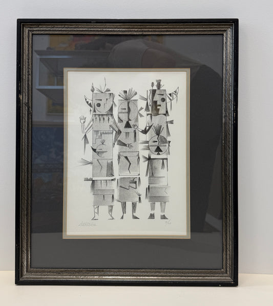 Framed black-and-white abstract drawing titled "Pueblo Spirits 3/20," featuring four geometric, humanoid figures with tribal elements, displayed against a white wall. The artwork is presented in framed dimensions of 17x20 inches.