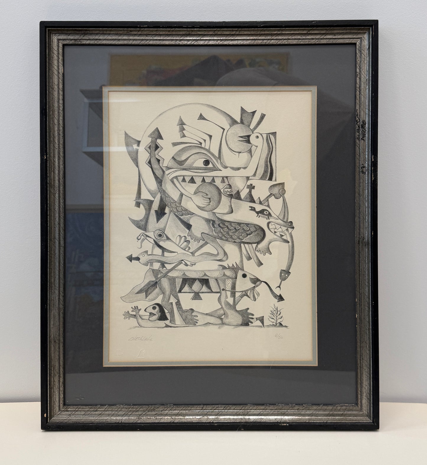 Framed "Pueblo Spirits 8/50" abstract black-and-white drawing featuring geometric and organic shapes, faces, and animal-like forms, displayed as sophisticated wall decor in a 17x20 frame against a plain wall.